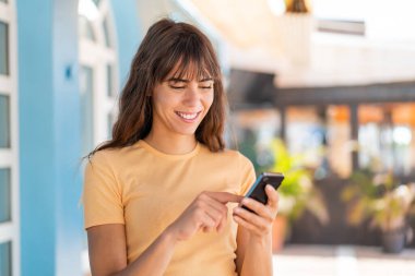 Dışarıdaki genç kadın cep telefonuyla mesaj ya da e-posta yolluyor.