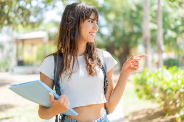 Açık havada genç bir bayan bir ürün sunmak için kenarı işaret ediyor.