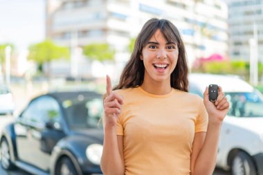Dışarıda arabanın anahtarlarını tutan genç bir kadın harika bir fikri işaret ediyor.