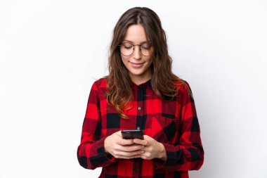 Beyaz arka planda izole edilmiş genç beyaz kadın cep telefonuyla mesaj gönderiyor.