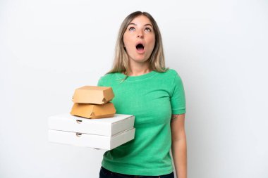 Genç Romen kadın elinde fast-food tutarken beyaz arka planda izole edilmiş yukarı bakıyor ve şaşırmış bir ifadeyle