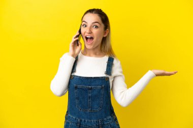 İzole edilmiş sarı arka planda cep telefonu kullanan genç bir kadın.