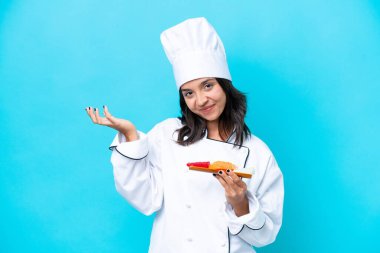 Mavi arka planda saşimi tutan genç İspanyol aşçı kadın davet etmek için ellerini yana uzatıyor.