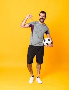 Futbol topuyla izole edilmiş sarı arka plan üzerinde tam boy bir adam fotoğrafı ve kendisiyle gurur duyuyor.