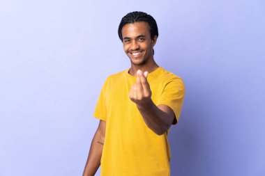 Örgülü genç Afrikalı Amerikalı adam mor arka planda izole edilmiş para hareketi yapıyor.