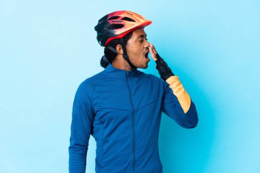 İzole edilmiş arka planda örgü ören genç bisikletçi esniyor ve ağzını eliyle açık tutuyor.