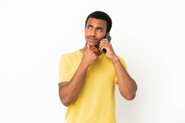 Afro-Amerikalı yakışıklı adam izole edilmiş beyaz arka plan üzerinden cep telefonu kullanıyor gülümserken yukarı bakıyor