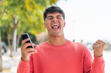 Dışarıda cep telefonu kullanan ve zafer jesti yapan genç bir İspanyol.