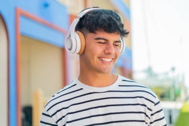 Genç İspanyol adam açık havada müzik dinliyor.