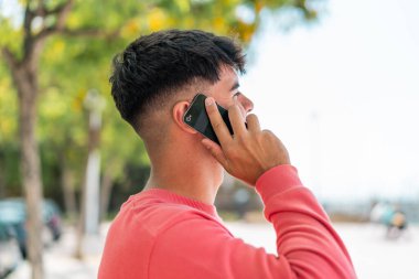 Dışarıdaki İspanyol genç adam cep telefonuyla birileriyle sohbet ediyor.