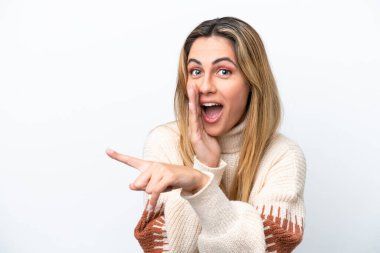 Beyaz arka planda izole edilmiş genç beyaz bir kadın bir ürünü sunmak ve bir şeyler fısıldamak için kenarı işaret ediyor.