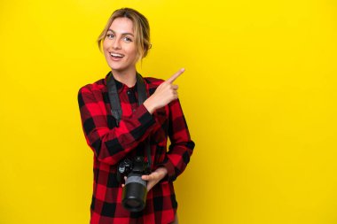 Uruguaylı fotoğrafçı kadın sarı arka planda izole edilmiş bir şekilde bir ürün sunmak için kenarı işaret ediyor.