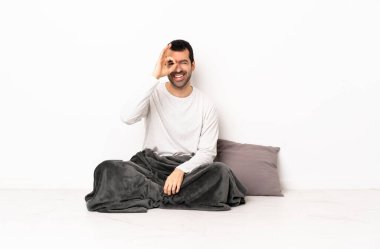 Pijamalı beyaz bir adam içeride yerde oturuyor. Parmaklarıyla 