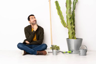 Bahçıvan içeride yerde oturuyor. Yukarı bakarken bir fikir düşünüyor.