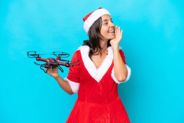 Anne Noel gibi giyinmiş genç bir kadın mavi arka planda izole edilmiş bir dron tutuyor ve ağzı sonuna kadar açık bağırıyor.