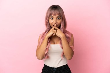 Pembe saçlı melez bir kadın. Pembe arka planda izole edilmiş. Sessizlik işareti gösteriyor.