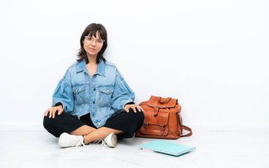 Genç bir kız öğrenci, beyaz arka planda tek başına oturmuş gülüyor.