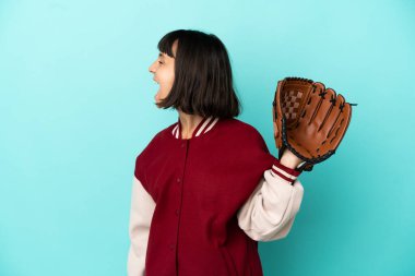 Beyzbol eldivenli genç melez kadın mavi arka planda izole edilmiş. Yan pozisyonda gülüyor.