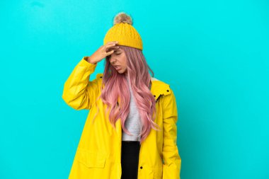 Pembe saçlı, yağmura dayanıklı bir ceket giyen, mavi arka planda başağrısı olan genç bir kadın.