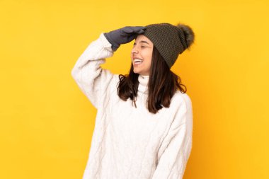Kışlık şapkalı genç bir kadın izole edilmiş sarı arka planda gülümsüyor.