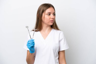 Beyaz arka planda izole edilmiş aletleri tutan dişçi kadın yan tarafa bakıyor