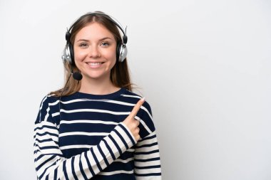 Beyaz arka planda izole edilmiş bir kulaklıkla çalışan beyaz pazarlamacı kadın bir ürünü sunmak için kenarı işaret ediyor.