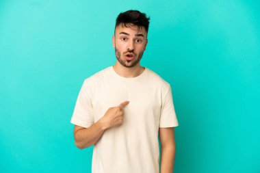 Mavi arka planda izole edilmiş genç beyaz adam kendini işaret ediyor.