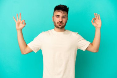 Zen pozisyonunda mavi arka planda izole edilmiş genç beyaz bir adam.