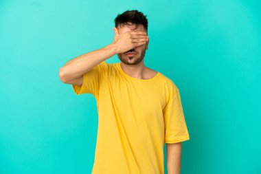 Genç beyaz adam mavi arka planda tek başına, gözleri elle kapatıyor. Bir şey görmek istemiyorum.