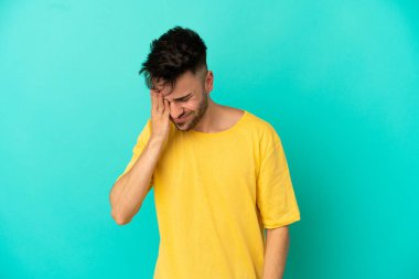 Kafkasyalı genç adam mavi arka planda izole edilmiş, baş ağrısı var.