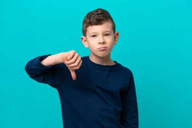 Küçük çocuk mavi arka planda izole edilmiş, başparmağını negatif ifade ile gösteriyor.