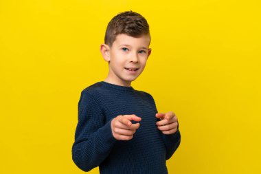 Sarı arka planda izole edilmiş küçük beyaz çocuk şaşırmış ve ön tarafı işaret ediyor.