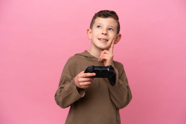 Küçük beyaz bir çocuk pembe arka planda izole edilmiş bir bilgisayar oyunu kontrolörüyle oynarken bir fikir arıyor.