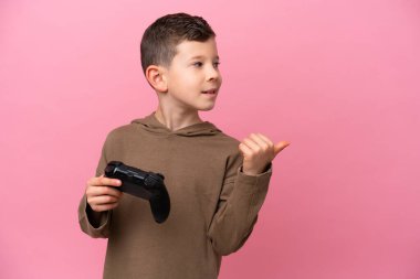 Pembe arka planda izole edilmiş bir bilgisayar oyunu kontrolörüyle oynayan beyaz çocuk bir ürünü sunmak için kenarı işaret ediyor.