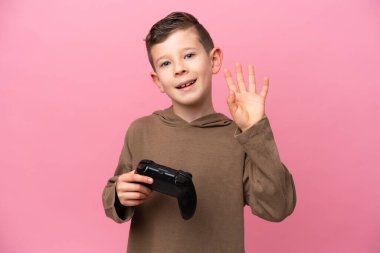 Pembe arka planda izole edilmiş bir bilgisayar oyunu kontrolörüyle oynayan beyaz çocuk mutlu bir ifadeyle selam veriyor.