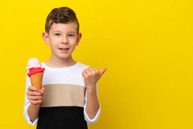 Sarı arka planda izole edilmiş kornet dondurması olan beyaz bir çocuk bir ürün sunmak için yan tarafı işaret ediyor.