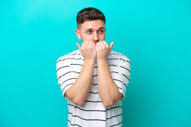 Mavi arka planda izole edilmiş genç beyaz bir adam gergin ve korkmuş bir şekilde elleriyle suni teneffüs yapıyor.
