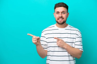 Kafkasyalı genç adam mavi arka planda izole edilmiş korkmuş ve kenarı işaret ediyor.