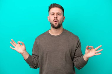 Zen pozisyonunda mavi arka planda izole edilmiş genç beyaz bir adam.