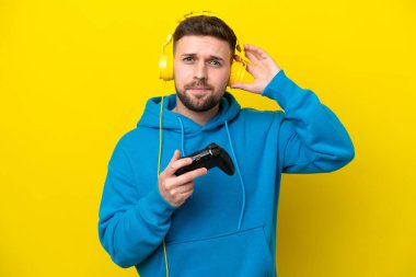 Sarı arka planda izole edilmiş bir bilgisayar oyunu denetleyicisiyle oynayan genç beyaz adamın şüpheleri var.