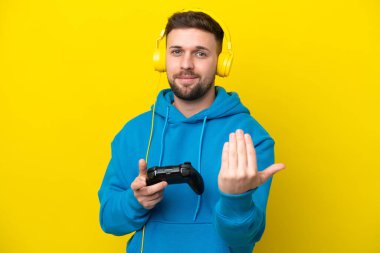 Sarı arka planda izole edilmiş bir bilgisayar oyunu kontrolörüyle oynayan genç beyaz bir adam elle gelmeye davet ediyor. Gelmene sevindim.