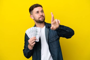 Kafkasyalı genç adam sarı arka planda izole edilmiş bir şekilde çok para alıyor ve şans diliyor.