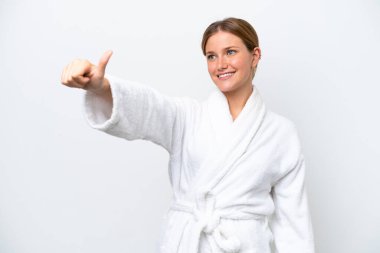 Bornozlu güzel sarışın kadın beyaz arka planda izole edilmiş bir şekilde baş parmak hareketi yapıyor.