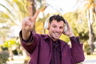 Genç beyaz adam açık havada müzik dinliyor ve şarkı söylüyor.