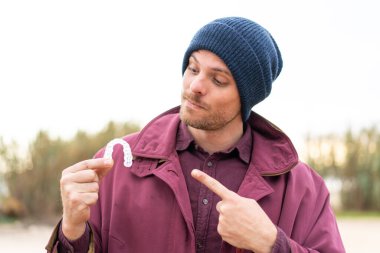 Genç beyaz adam dışarıda görünmez diş telleri tutuyor.