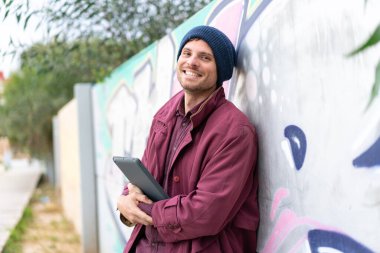 Açık havada elinde tablet tutan genç beyaz bir adam.