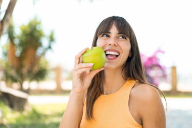 Açık havada elinde mutlu bir ifadeyle elma tutan genç bir kadın.