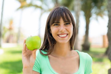 Açık havada elmalı genç bir kadın çok fazla gülümsüyor.