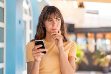 Dışarıda cep telefonu kullanan ve düşünen genç bir kadın.