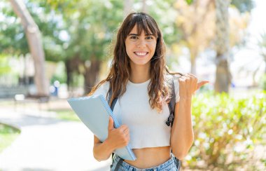 Açık havada genç bir bayan bir ürün sunmak için kenarı işaret ediyor.